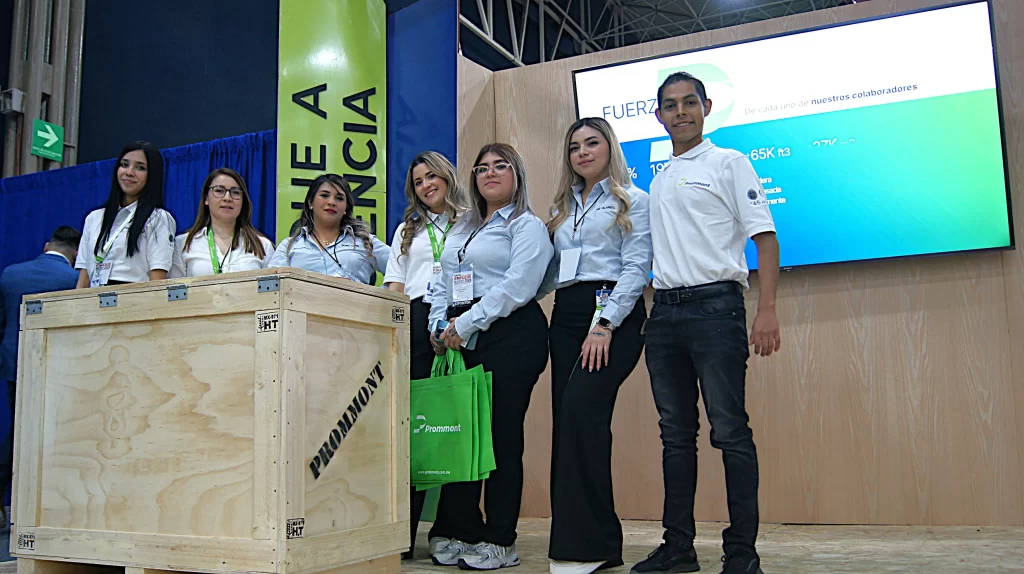Colaboradores de la empresa vestidos de blanco posando junto a una de las cajas de madera de Prommont en un stand